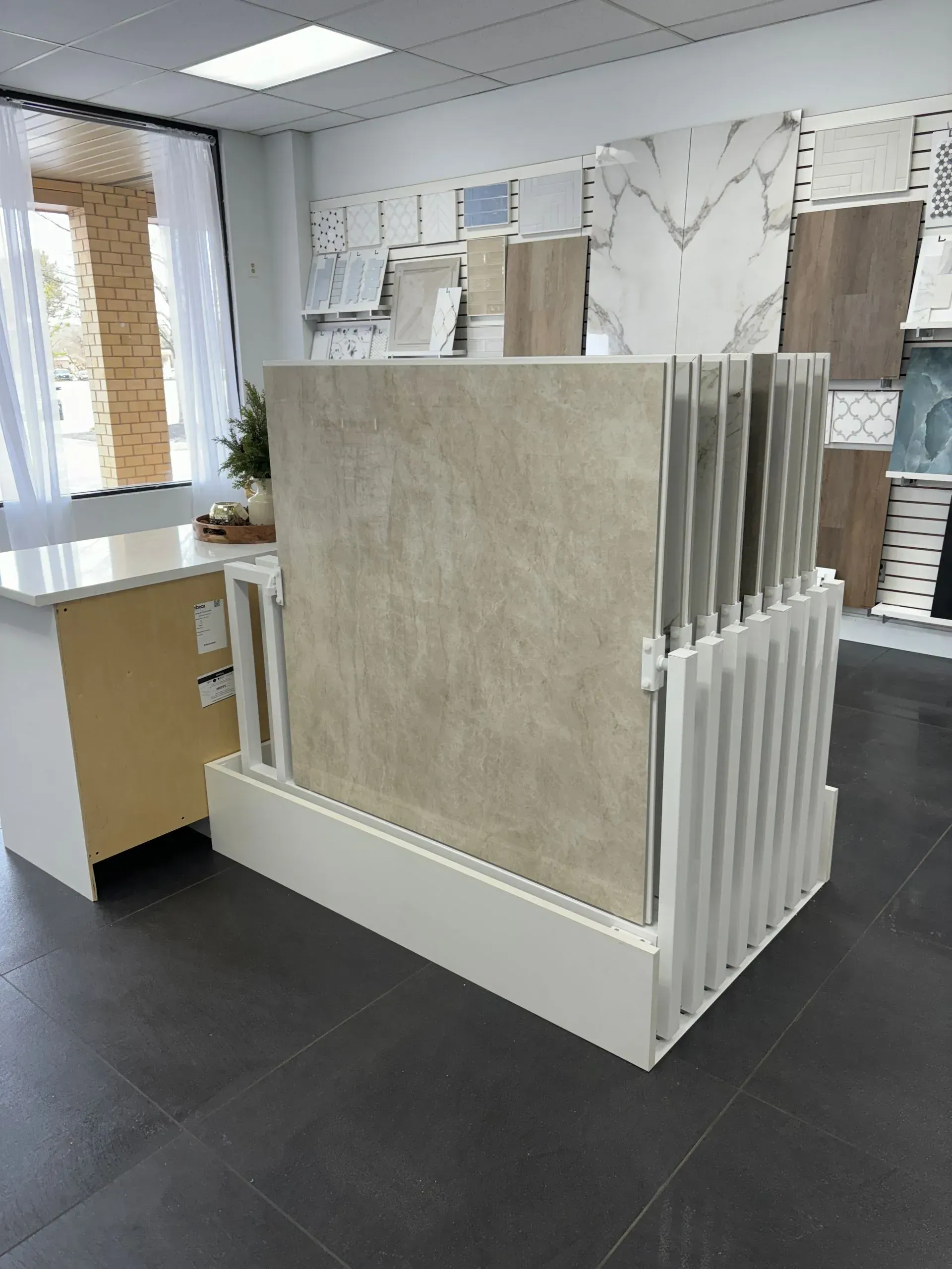 Tile display rack in a showroom with beige and white samples on a dark floor.
