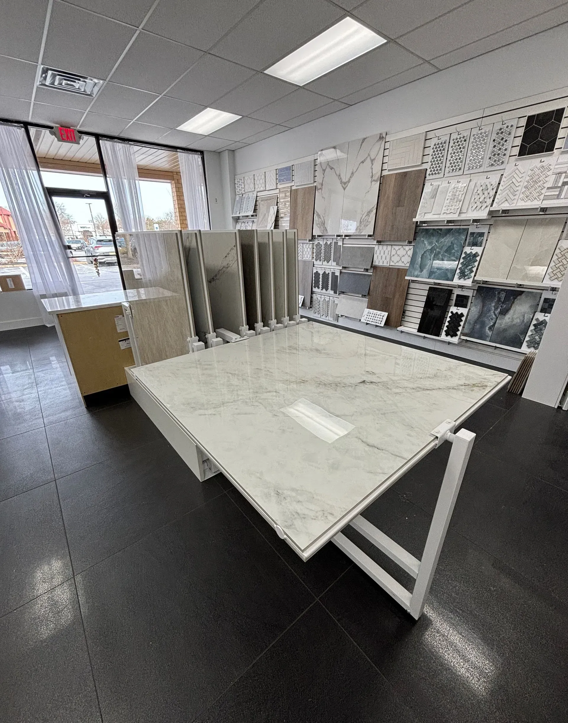 Inside a tile showroom, a white display table sits among stacked sample boards and flooring materials.