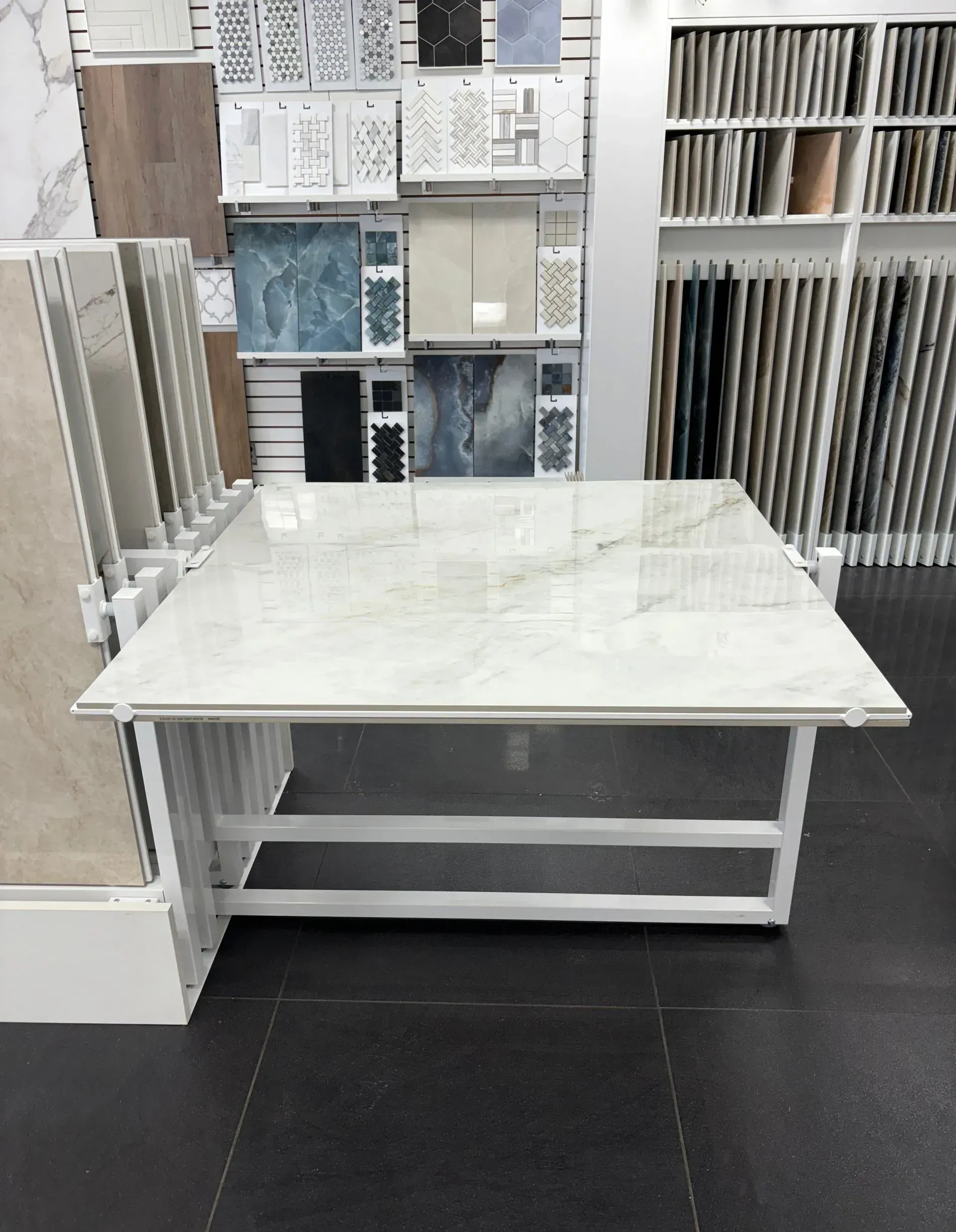 White marble-top display table in a tile showroom, with sample tiles and flooring displays behind it.