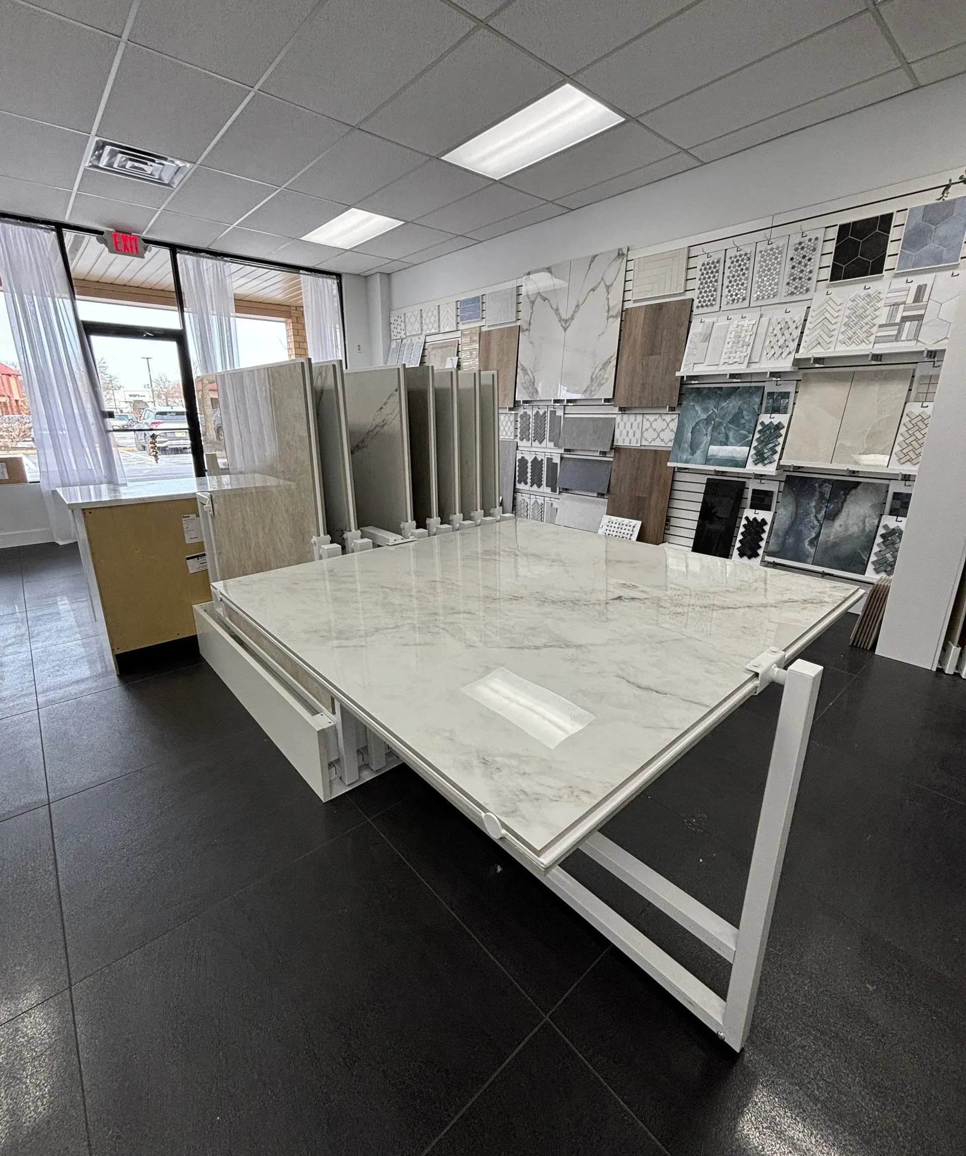 Modern showroom with a white display table, black floor, and wall samples of tiles and materials.