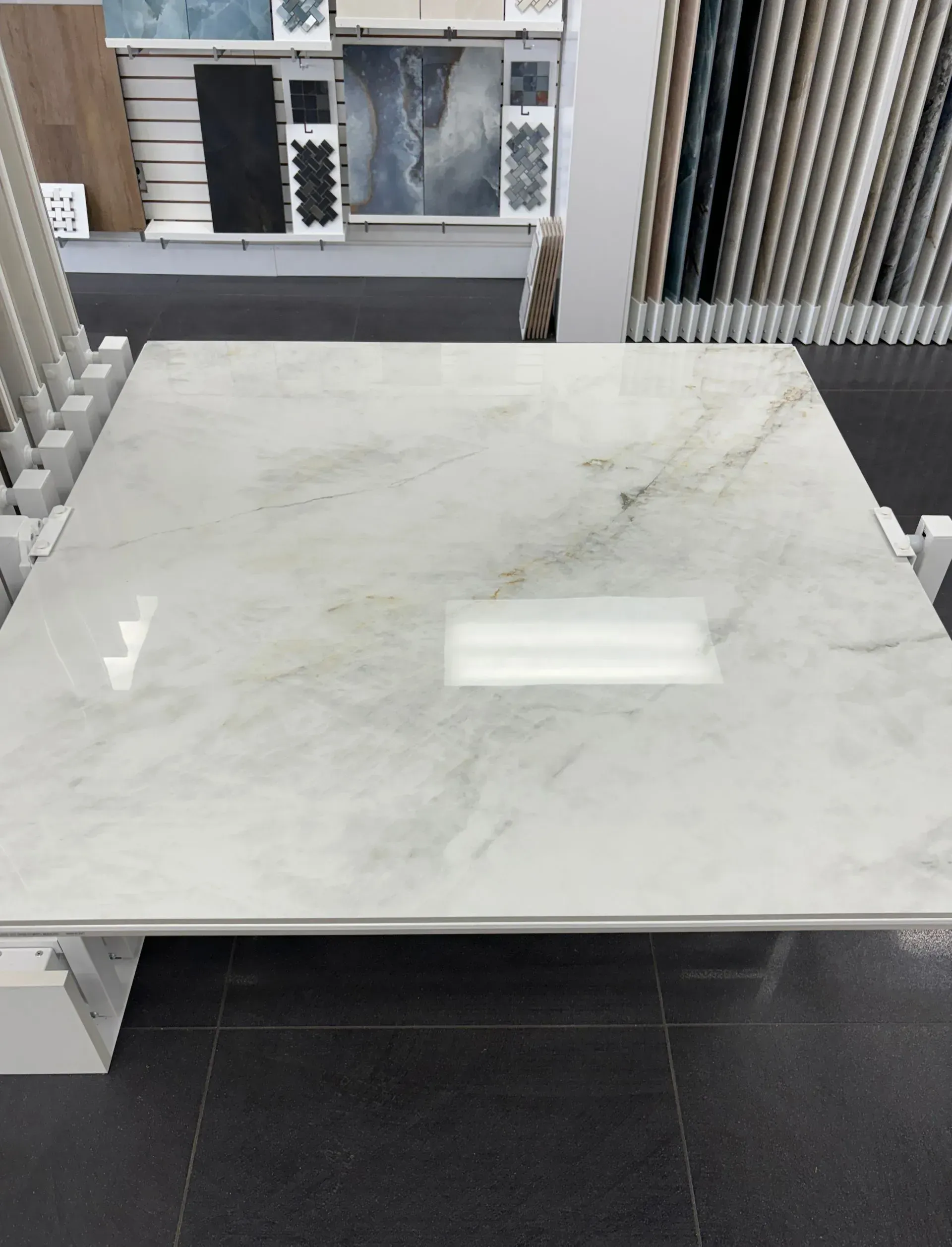 Marble-topped square table in a showroom with black tile floor and window displays behind it