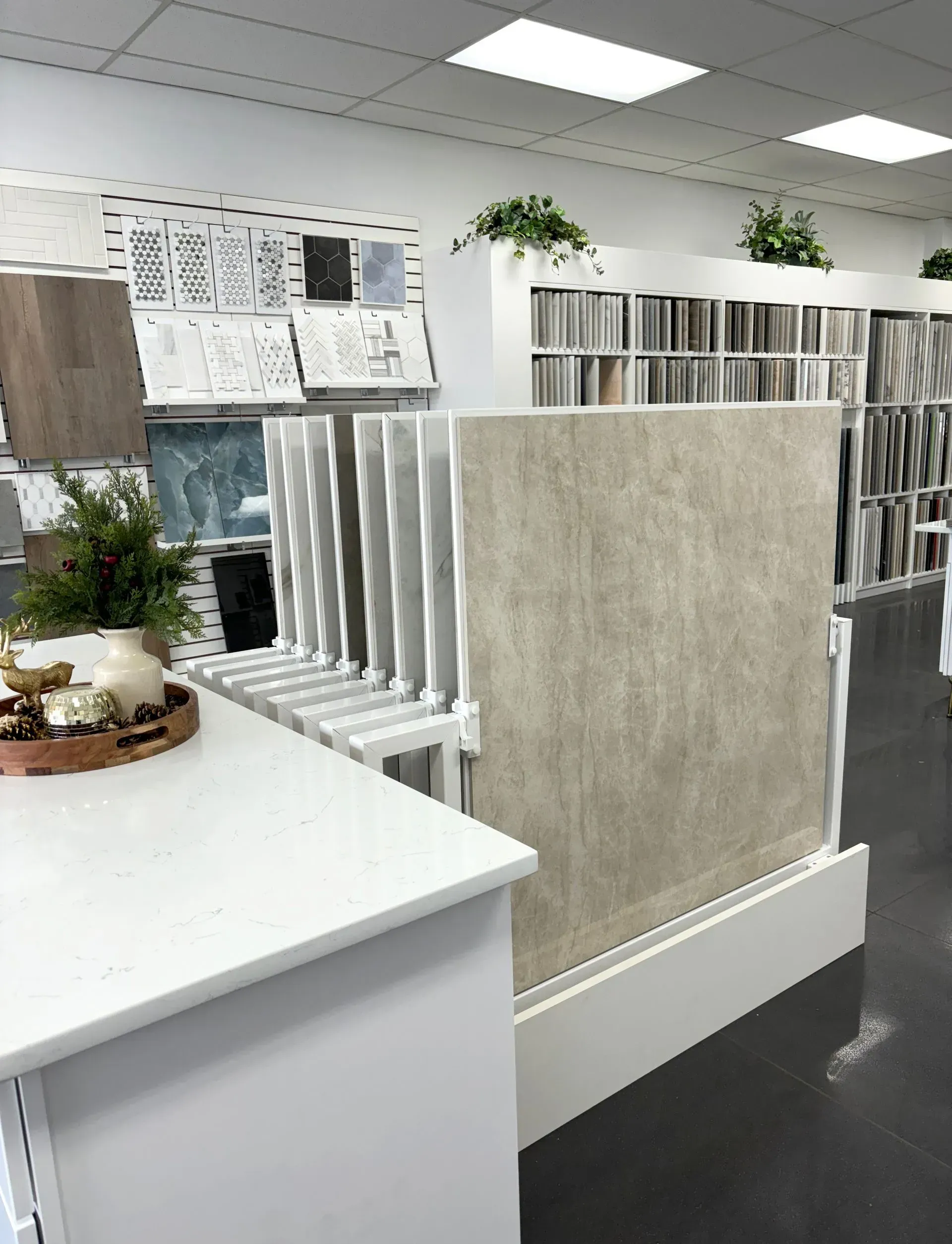 Office with cubicle dividers, desks, shelves, and plants under bright ceiling lights.