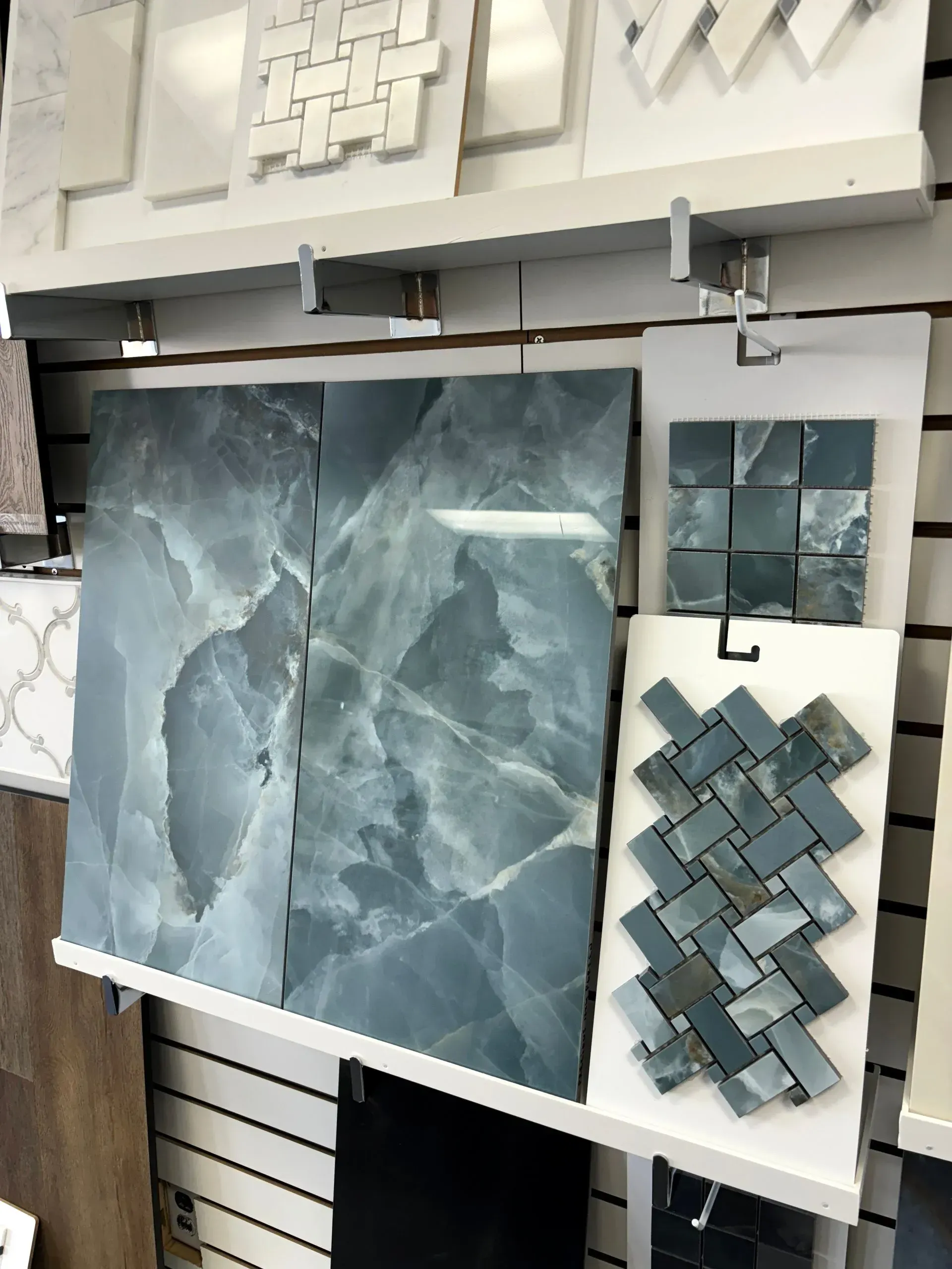 Tile display with large blue-gray marble slabs, mosaic samples, and white wall panels in a showroom.