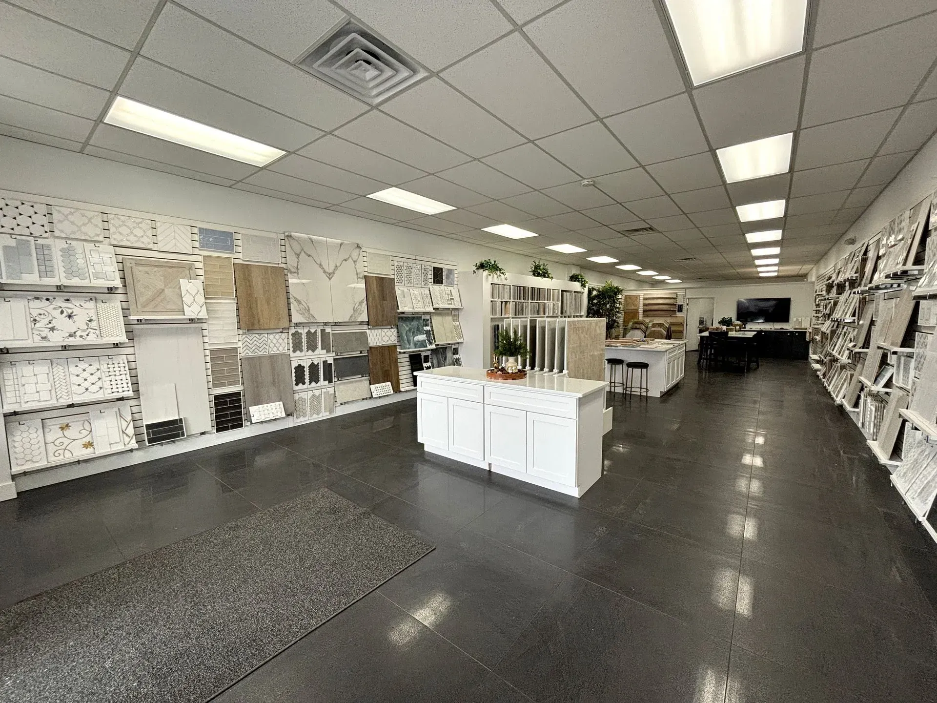Wide retail showroom with flooring samples, cabinets, and displays under bright ceiling lights