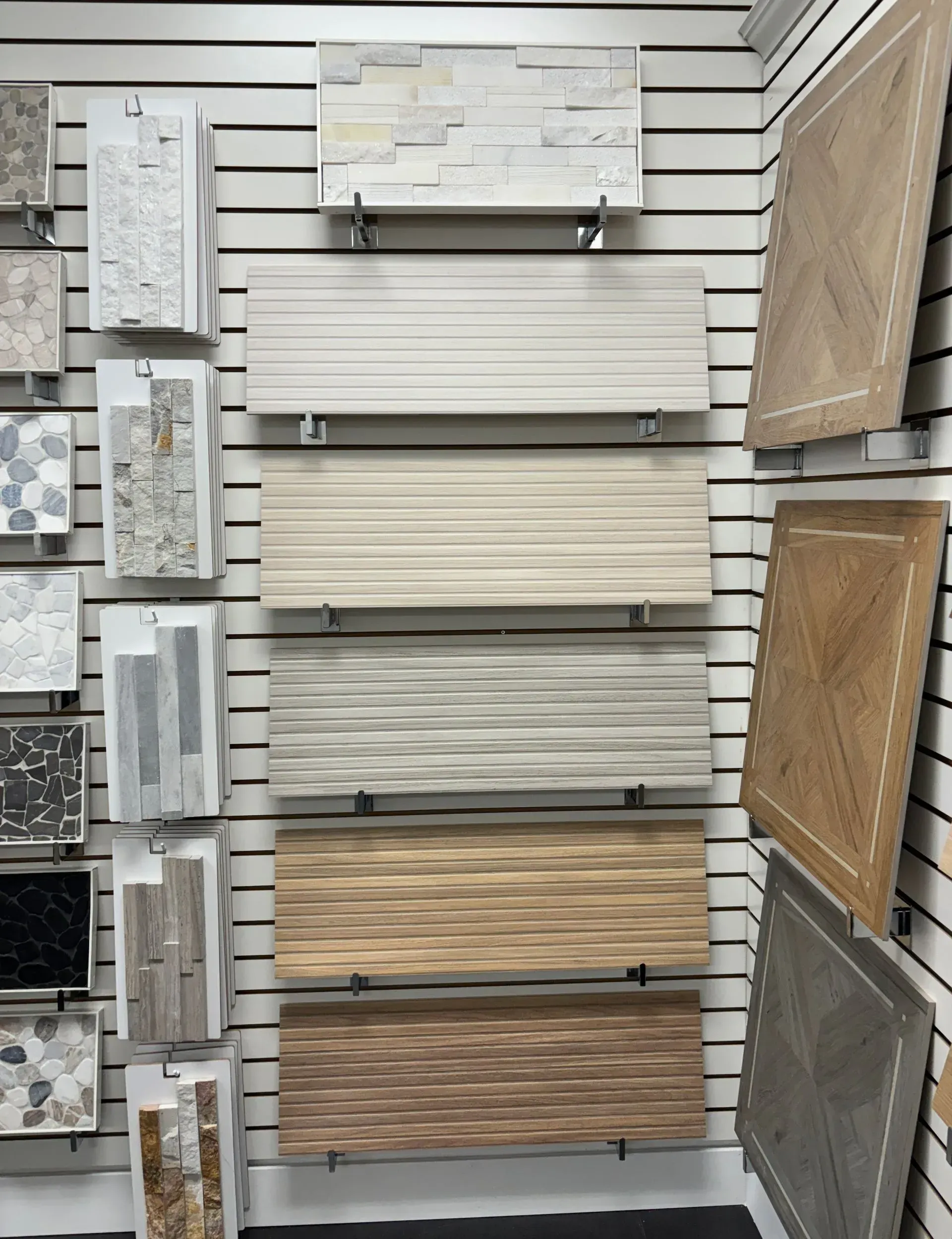 Display of assorted wall tiles and samples in a showroom, mostly beige, gray, and wood tones.