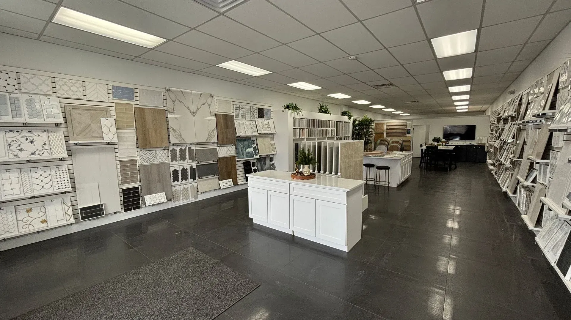 Bright flooring showroom with white cabinets, tile displays, and ceiling lights in a wide aisle