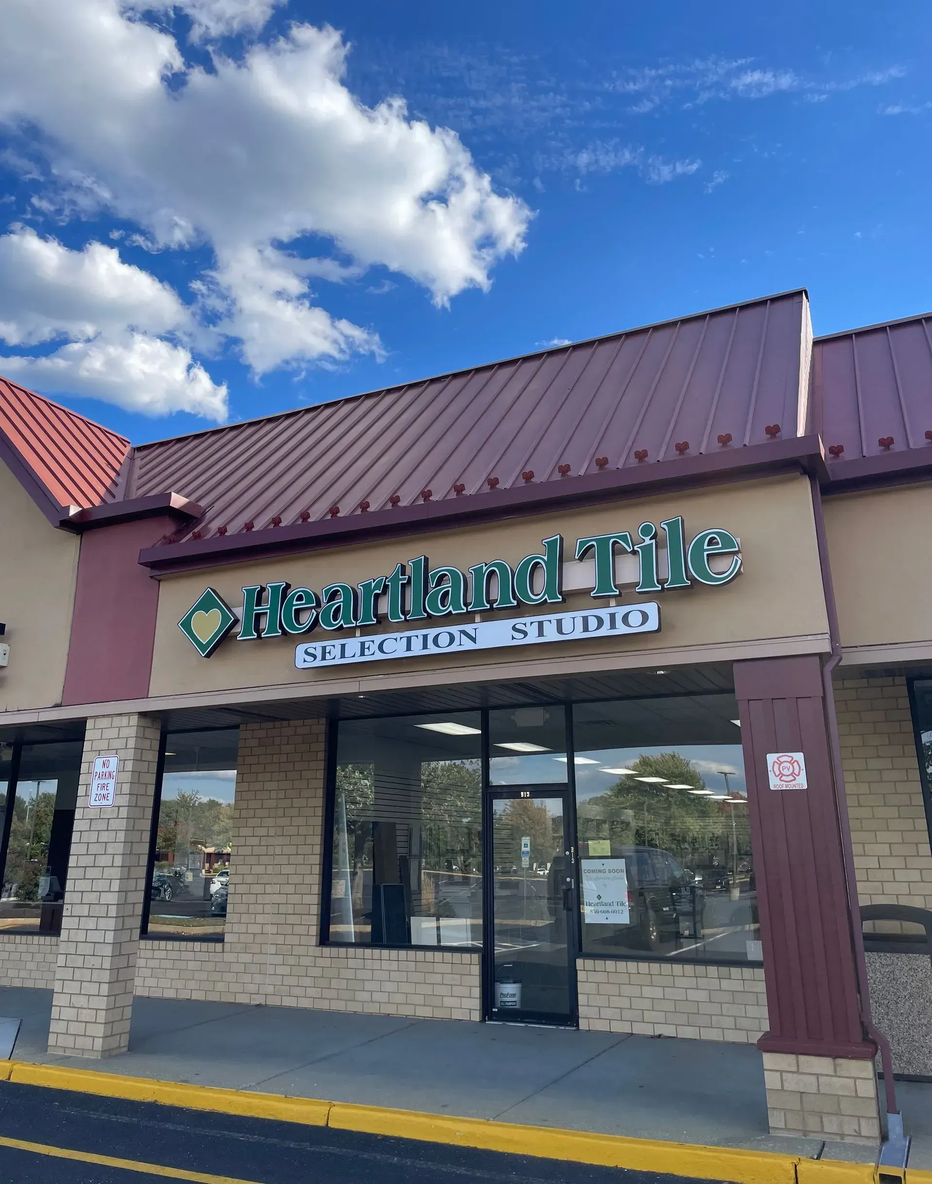 Restaurant exterior with stone facade, glass doors, and green sign under a blue sky with clouds