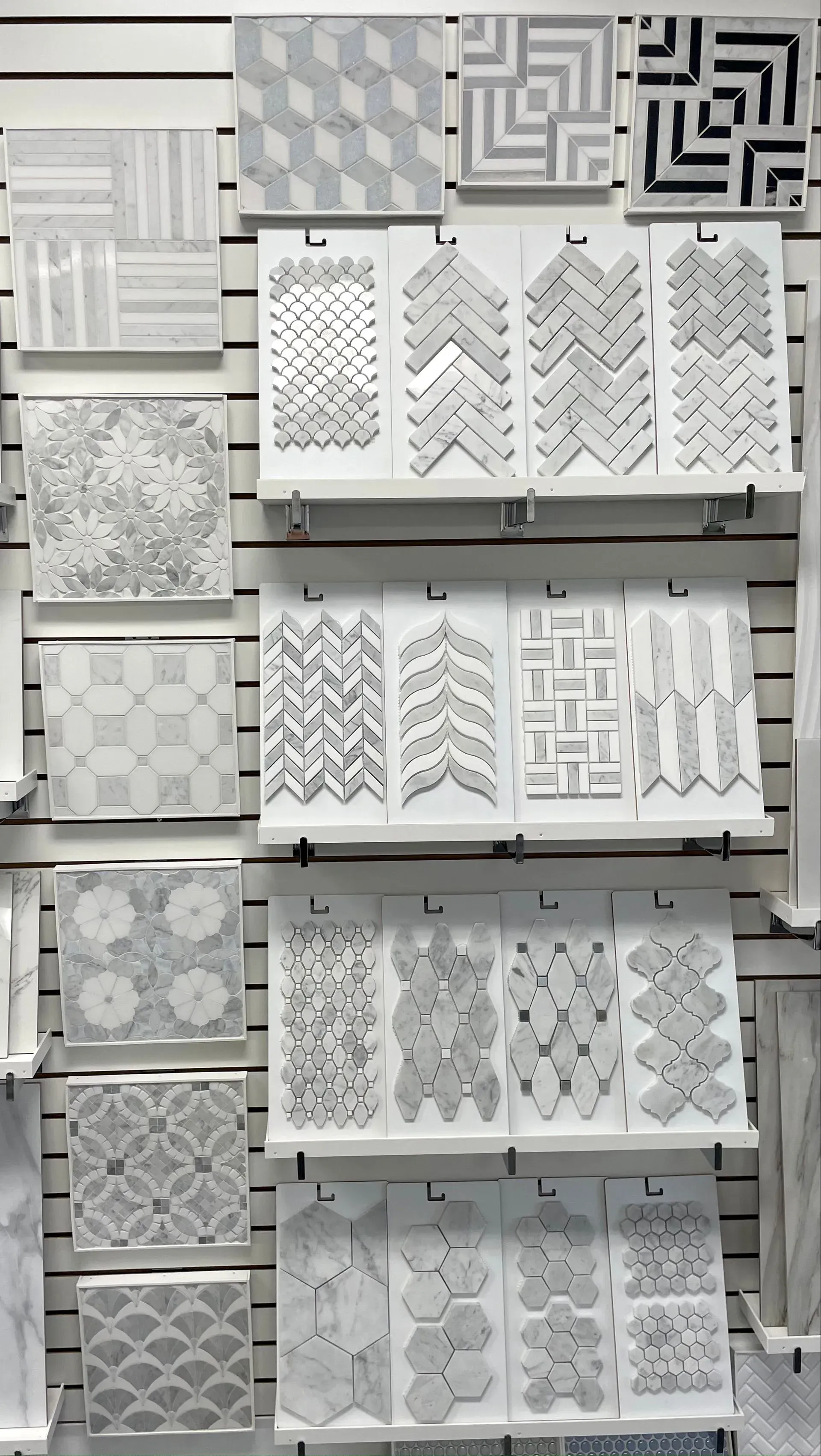 Display of white and gray decorative tile samples on a store wall, in assorted patterns and textures