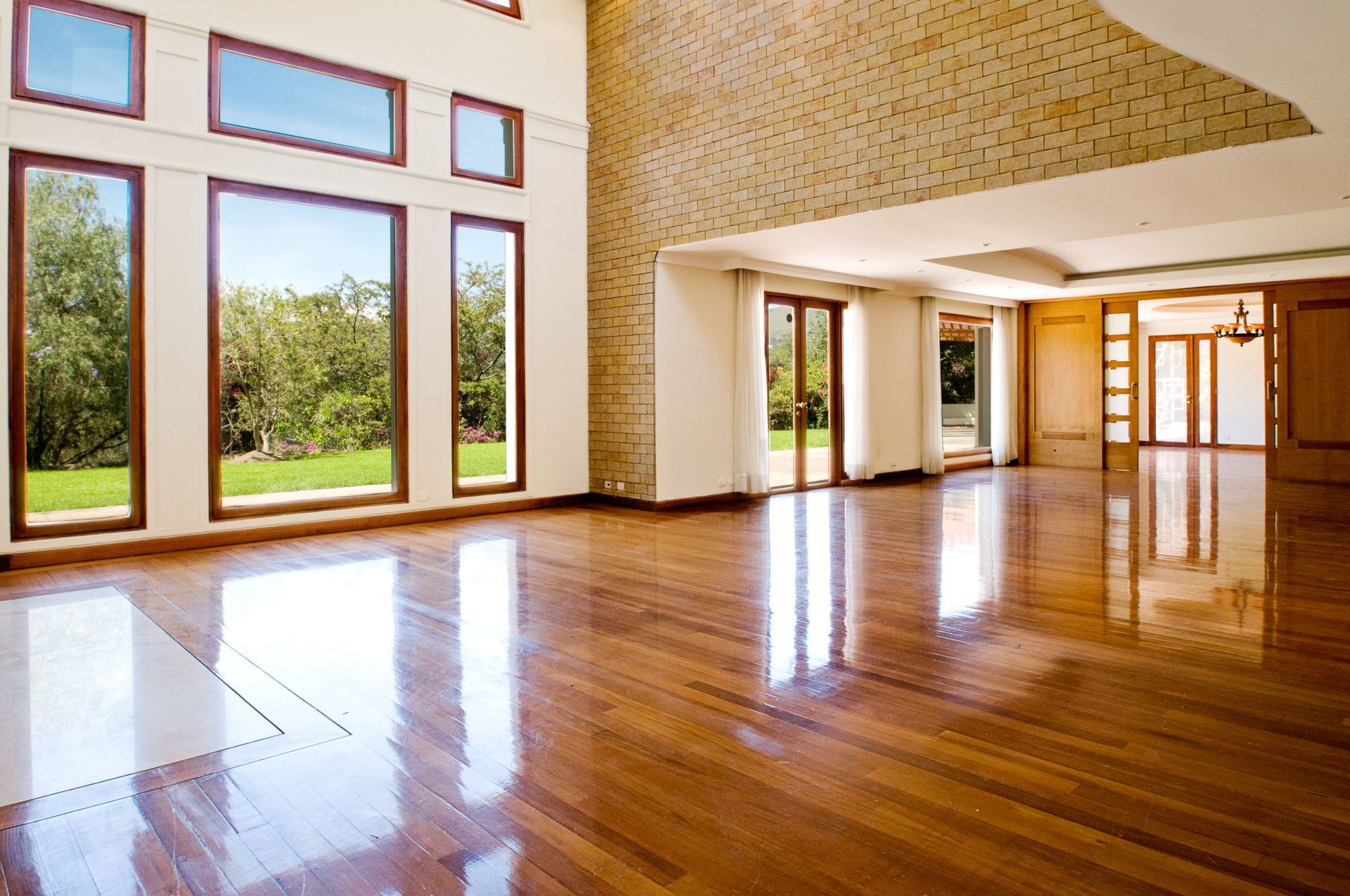 Empty modern room with hardwood floors, large windows, and sunlight streaming in