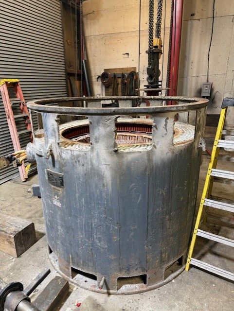 Large rusted metal industrial tank in a workshop, with open top and worn gray-blue exterior.