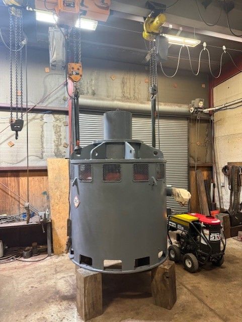 Gray industrial machine on wooden blocks in a workshop, with a red ATV and overhead hoist in the background