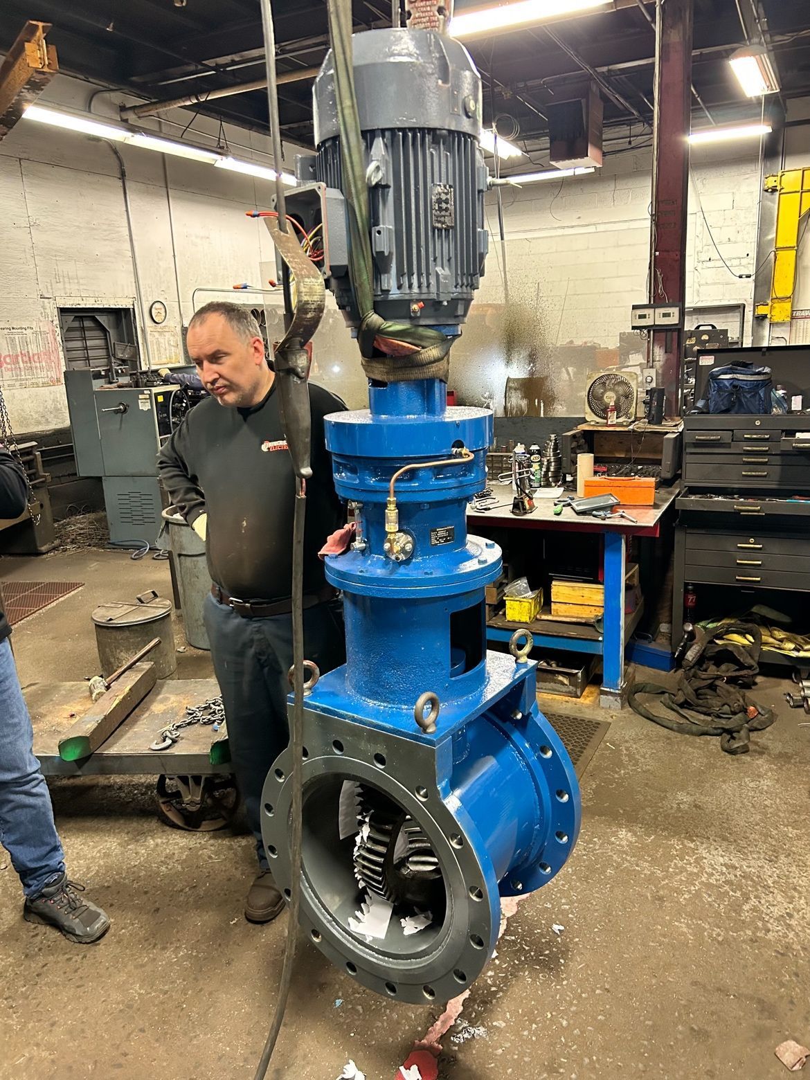 Large blue industrial valve assembly being inspected in a workshop, with a man standing beside it.