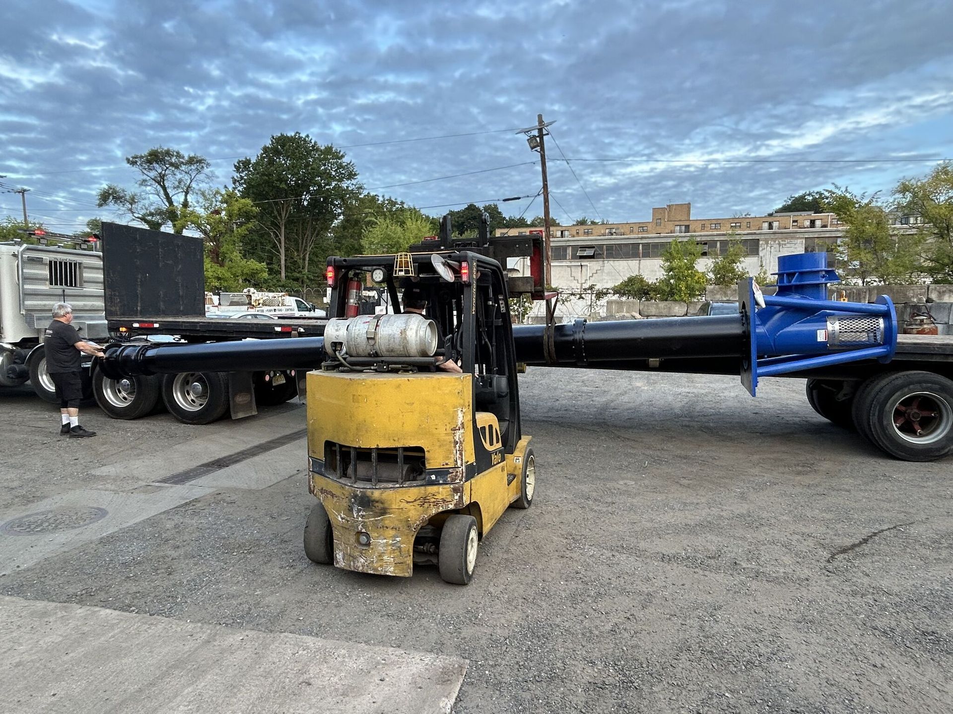 Yellow forklift in front of two flatbed trailers in an industrial yard.