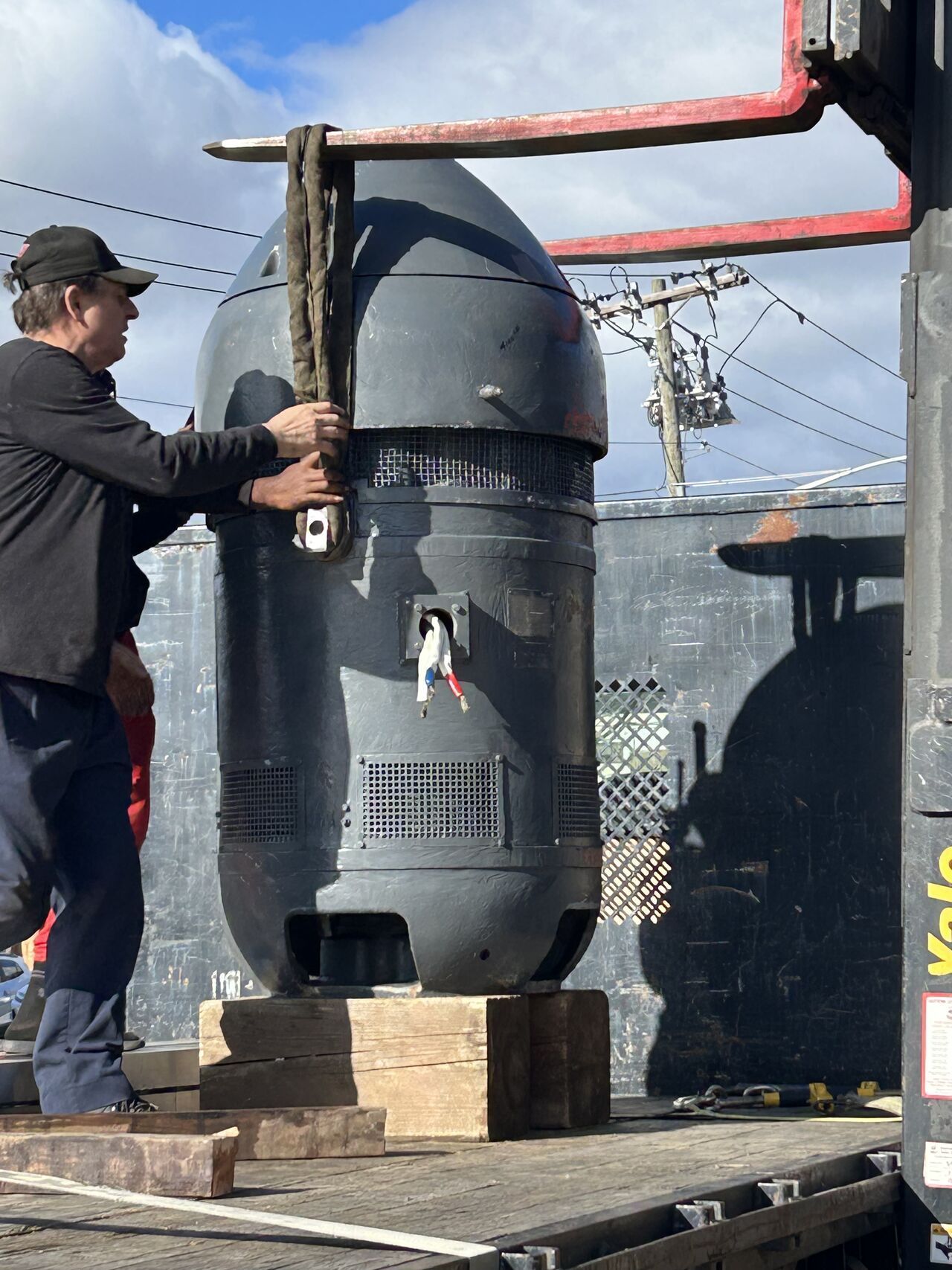 Worker beside large black industrial tank outdoors, adjusting a valve on a wooden base.
