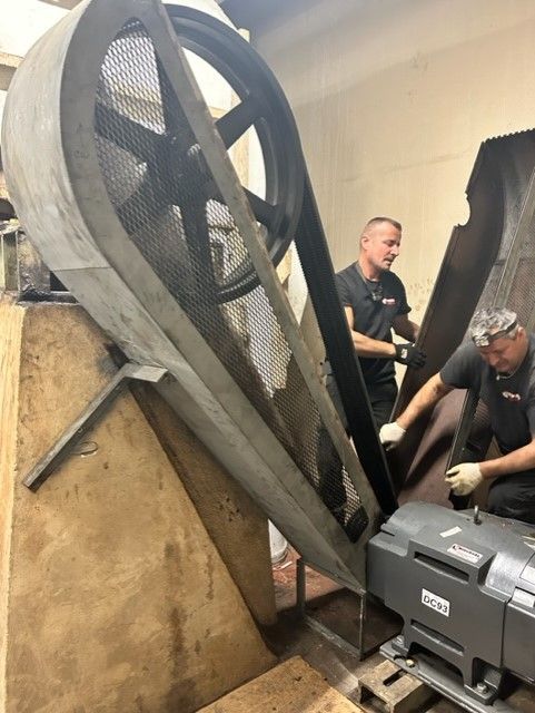 two people wearing black working on a huge machine