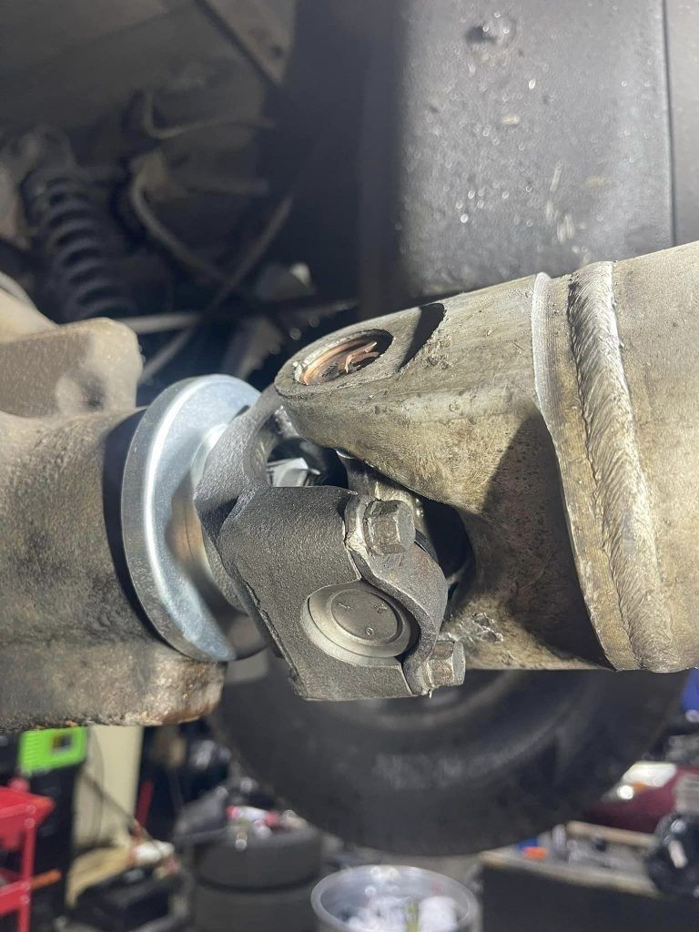 U-joint connecting two shafts. Metal components with grease and visible bolts, under vehicle.