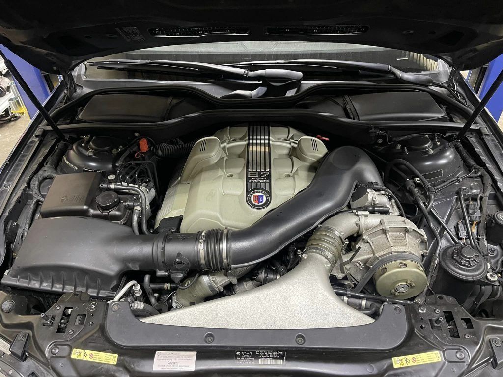 Engine bay of a black car with a large, beige engine and black intake tubing.