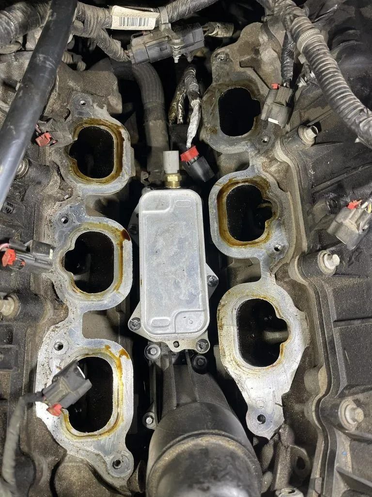 Engine with removed intake manifold, oil cooler visible between cylinder heads, black and brown.