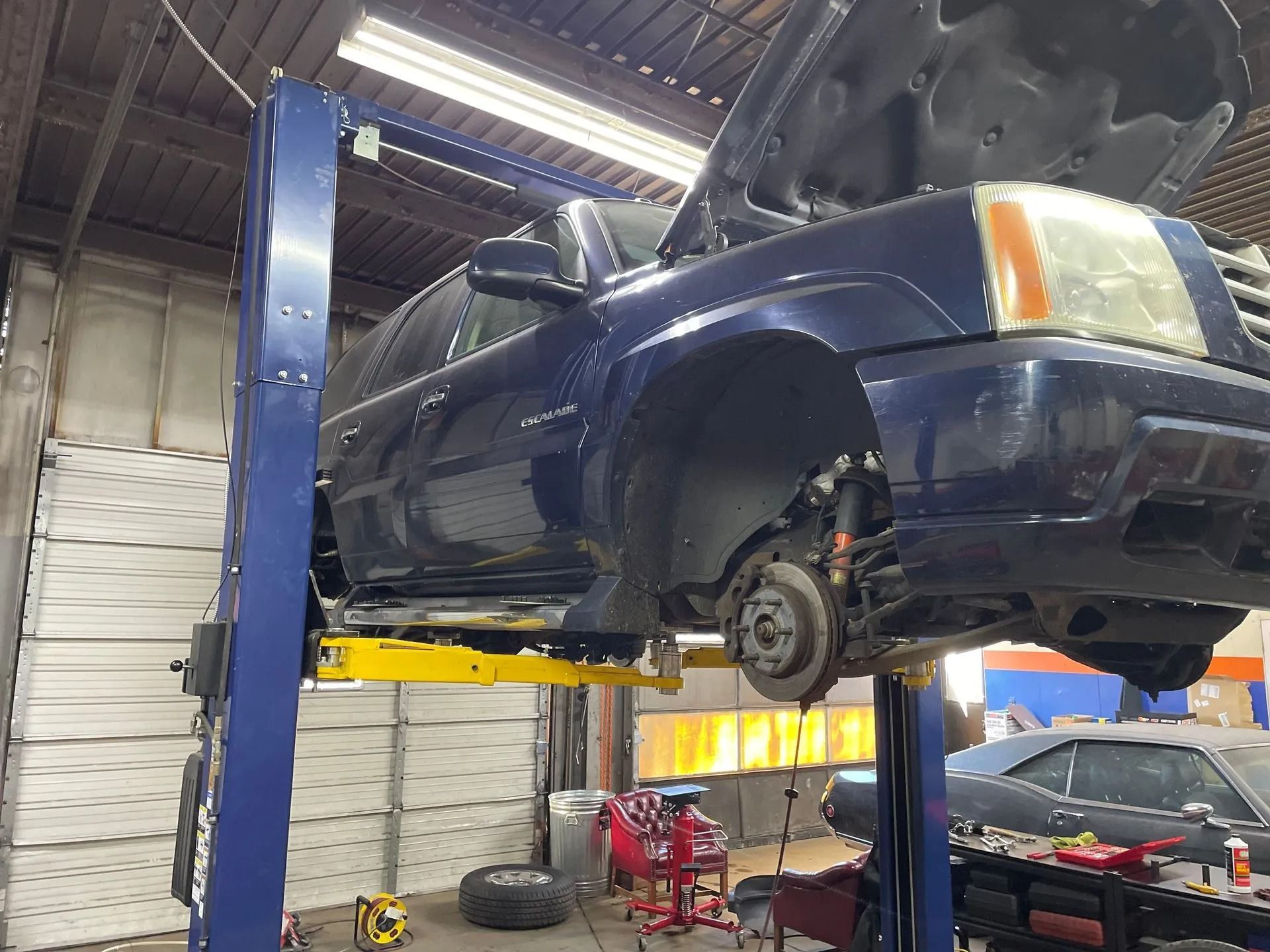 Blue SUV on a car lift in a garage with the hood up, front tire removed.