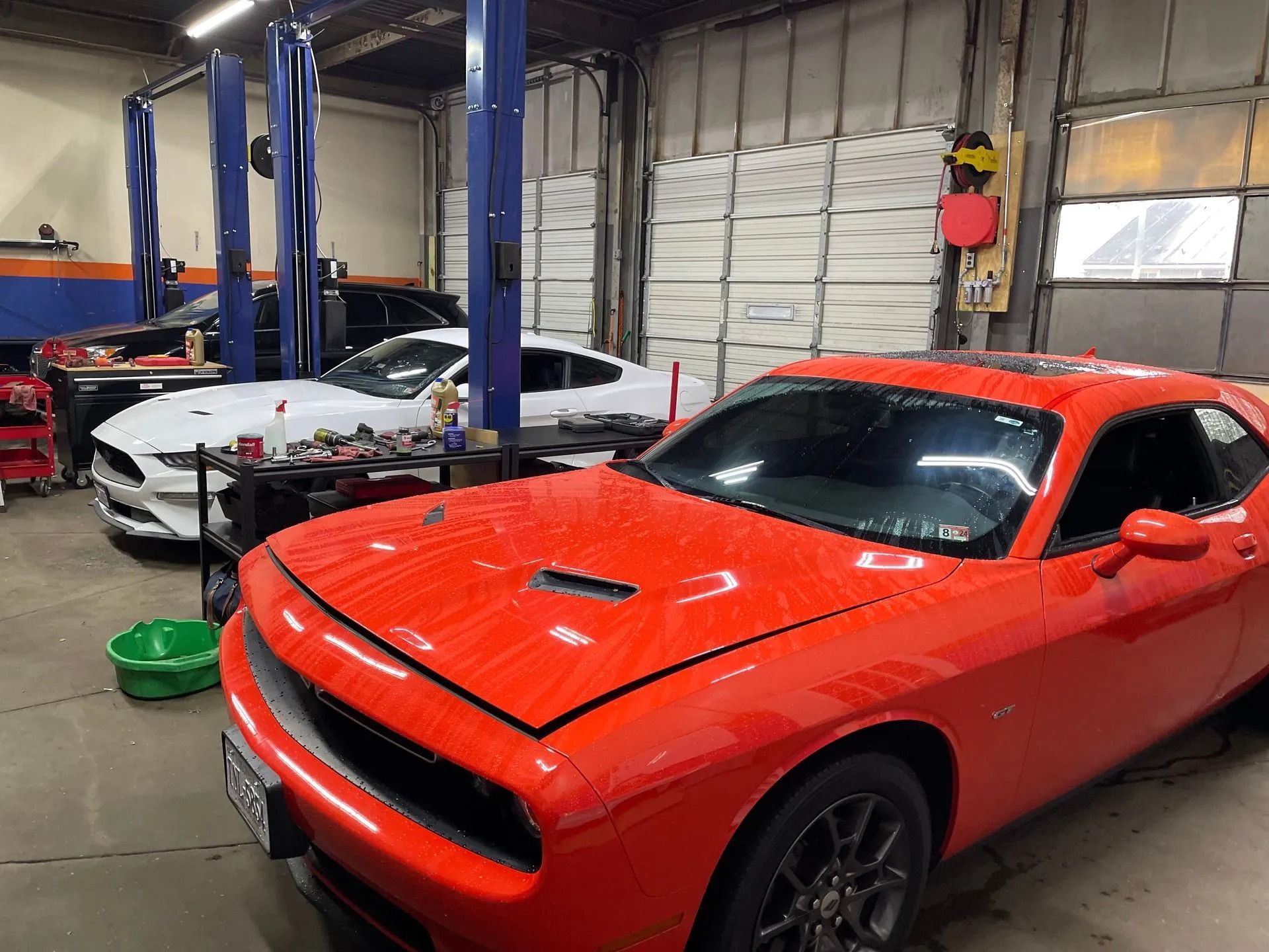 Red Dodge Challenger in auto repair shop with white Ford Mustang in background.