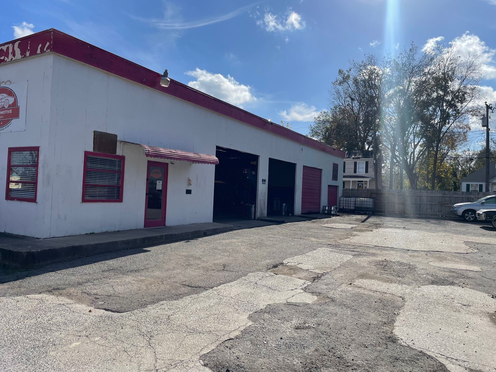 White commercial building with red trim, garage bays, and a cracked asphalt parking lot under a blue sky.