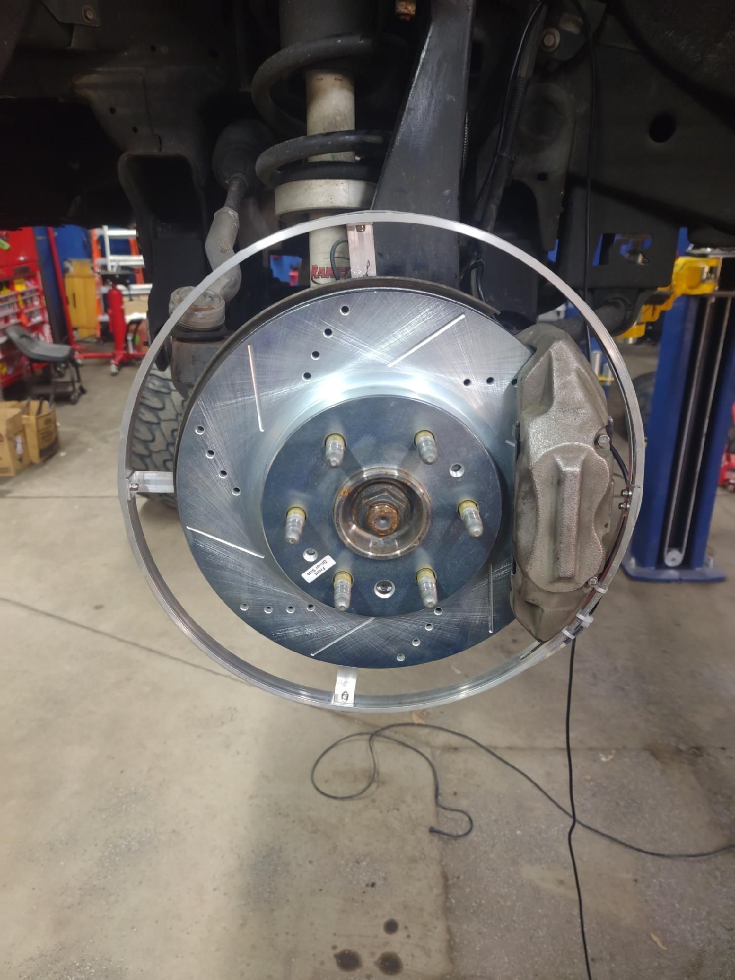 Brake rotor and caliper assembly on a vehicle, showing a silver rotor with drilled holes and a gray caliper.