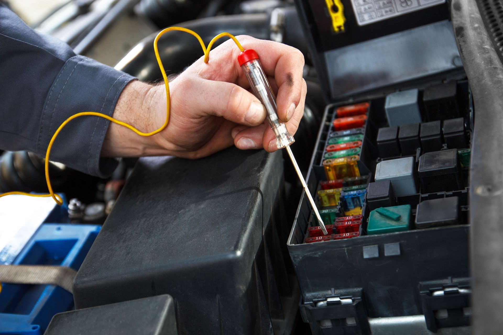Hand holding a test light checking car fuses in a black fuse box.