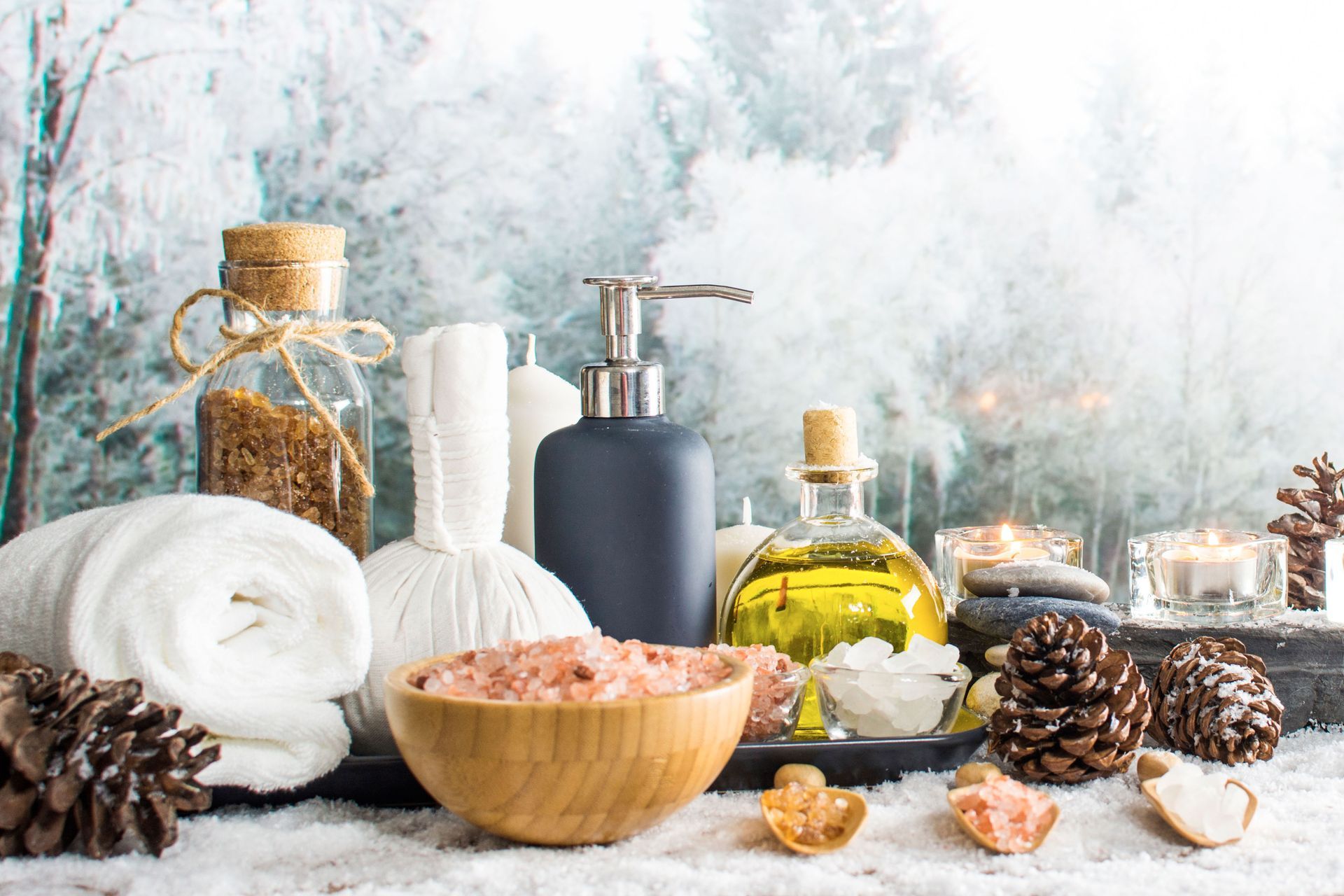 A table topped with bottles, towels, candles, and pine cones