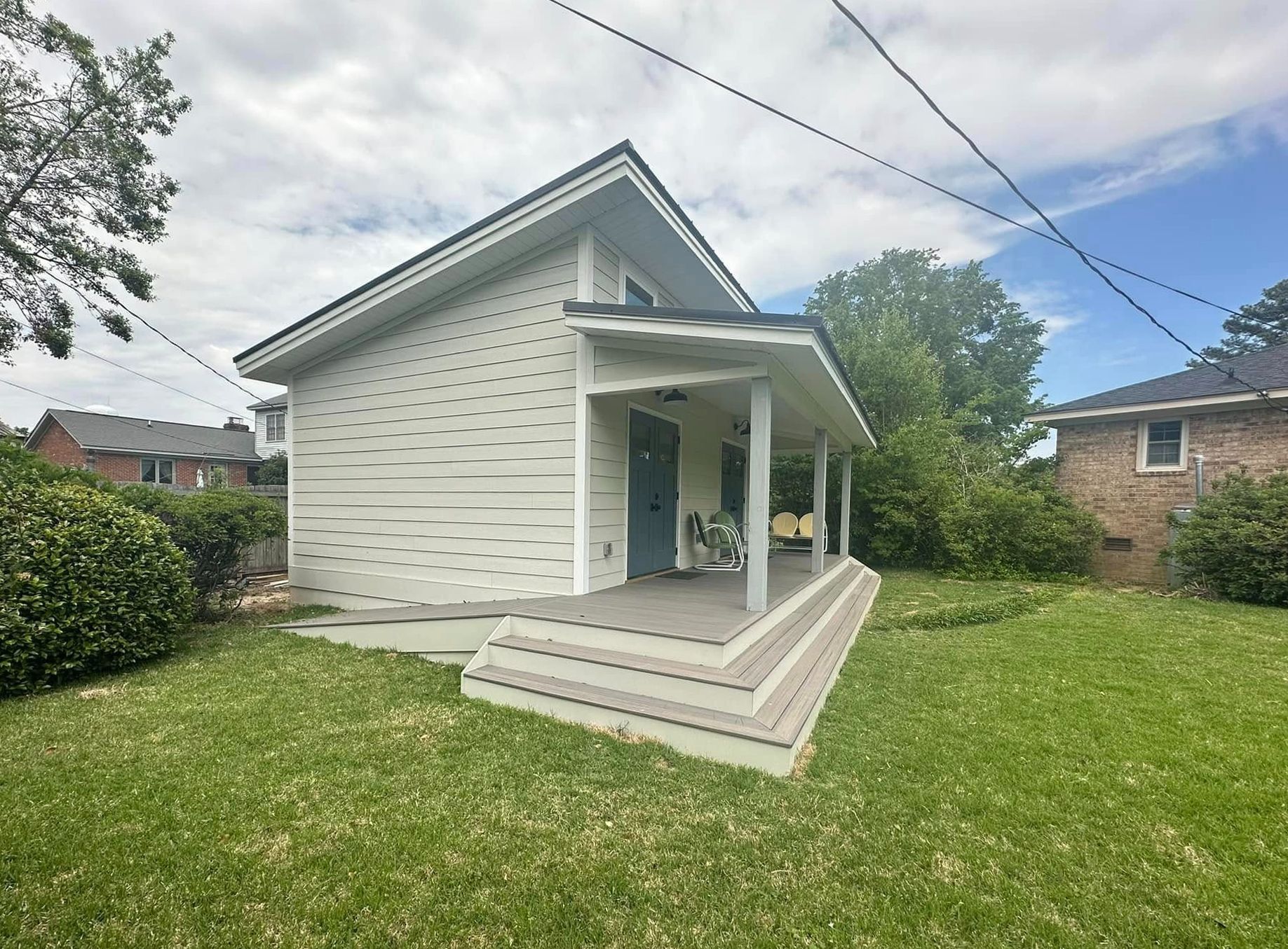 Small light-colored house with a porch, steps, and green lawn on a partly cloudy day.