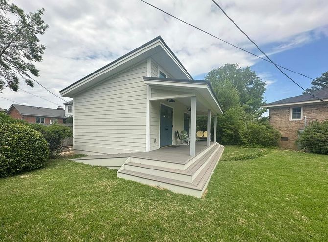 Small light-colored house with a porch, steps, and green lawn on a partly cloudy day.
