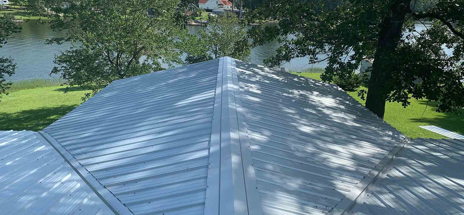 View of a white metal roof with trees and a lake in the background.