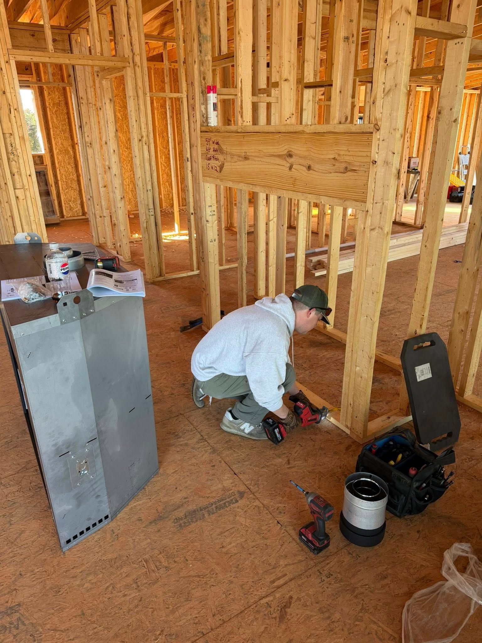 Construction worker installs something on the floor in a wood-framed building.