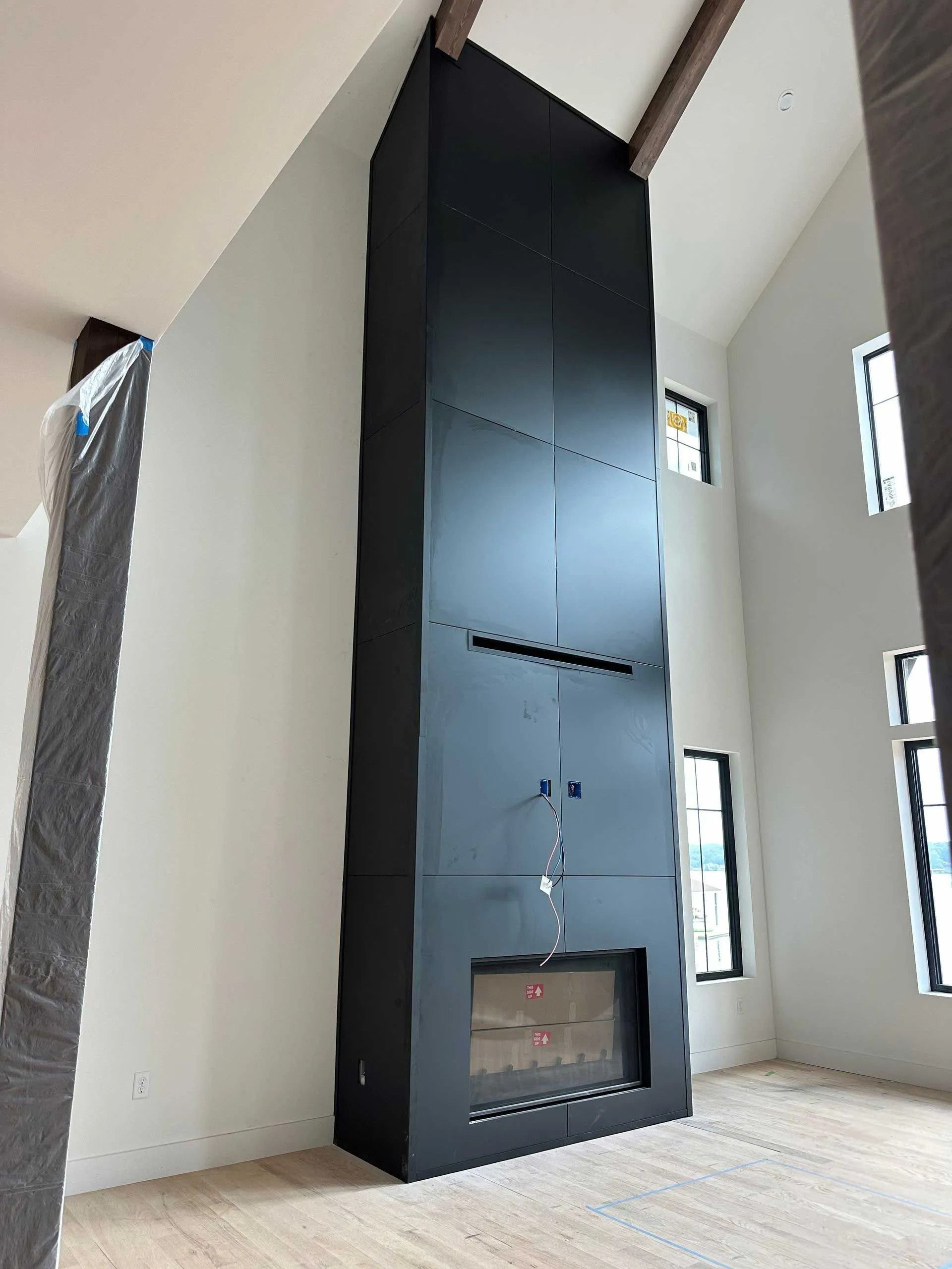 Tall black fireplace against white walls, wood beams, and small windows.
