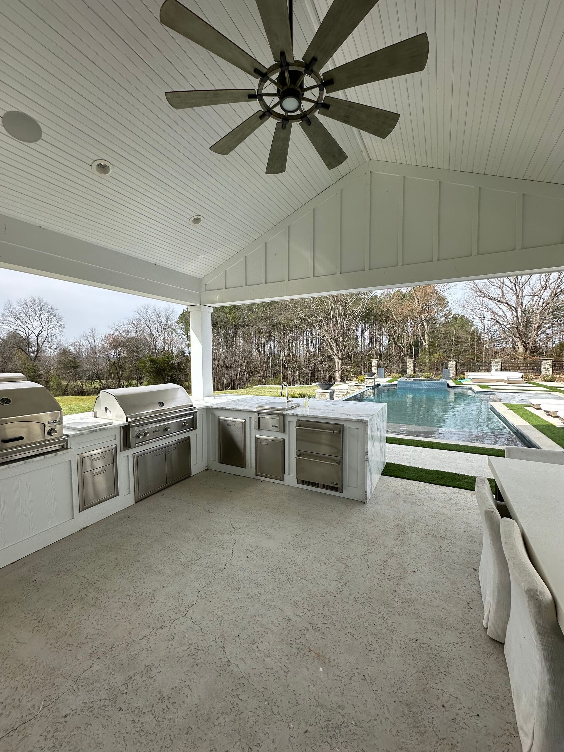 Outdoor kitchen with stainless steel appliances, concrete countertops, and a pool view.