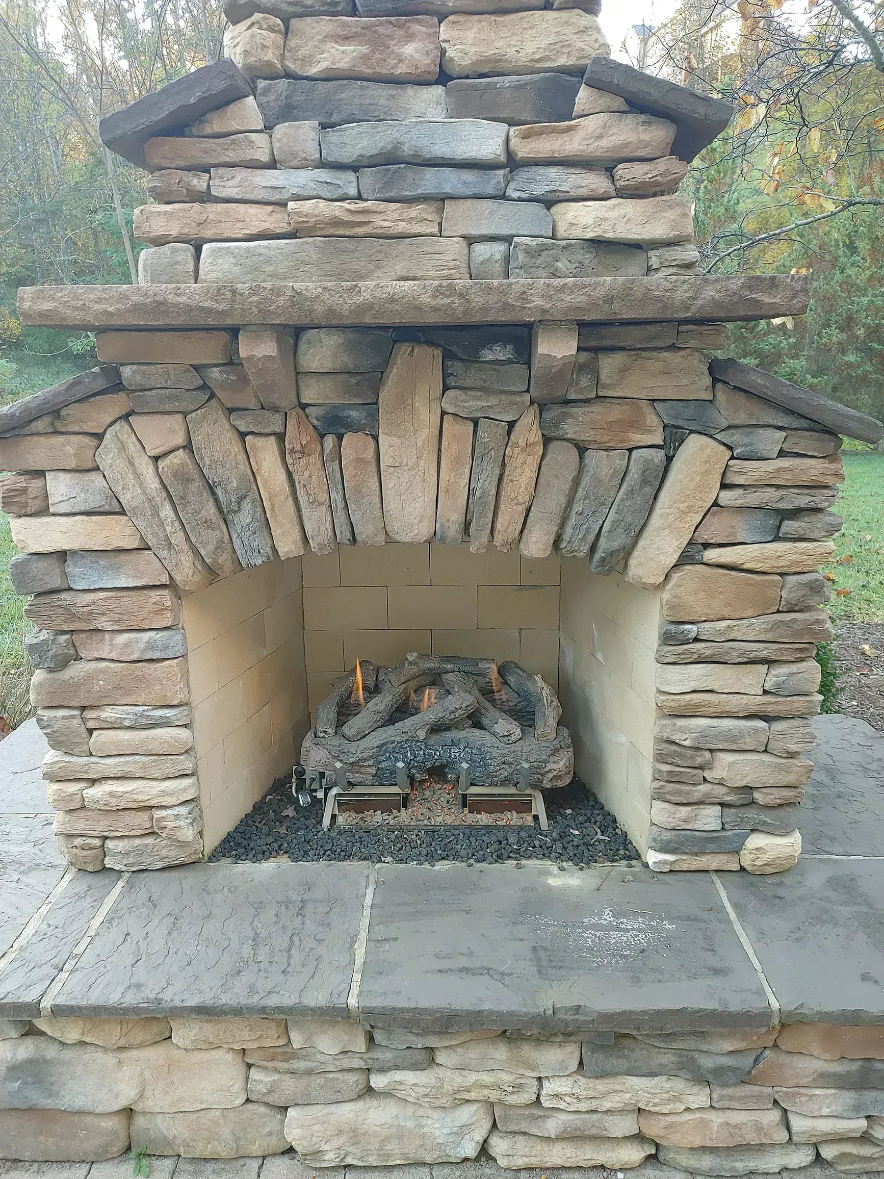Outdoor stone fireplace with a glowing gas fire.