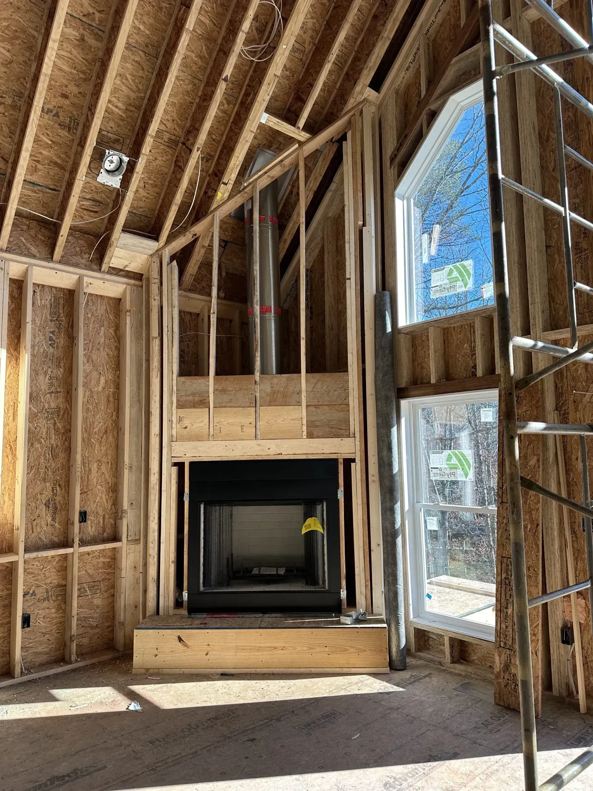 Interior of a house under construction; a fireplace is framed by wooden studs, chimney visible.