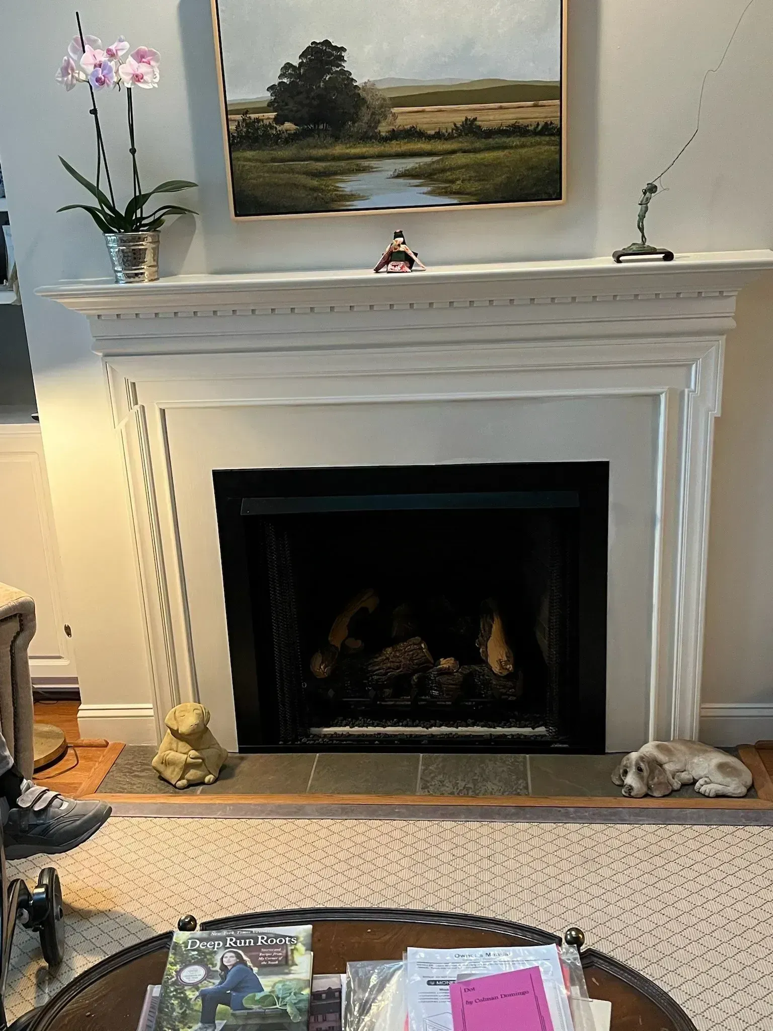 Fireplace with artwork, orchid, and small sculptures on mantle.