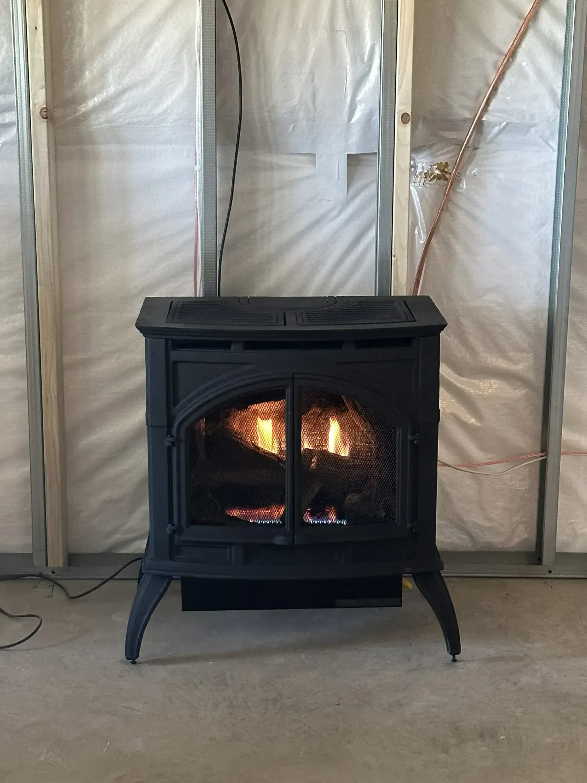 Black gas fireplace lit against a wall under construction.