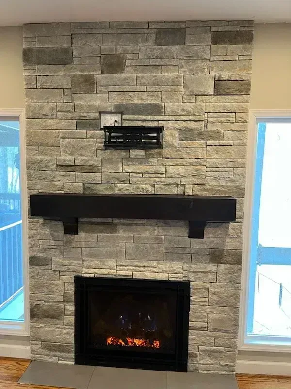 Fireplace with gray stone facing, black mantel and firebox, with a TV mount above.