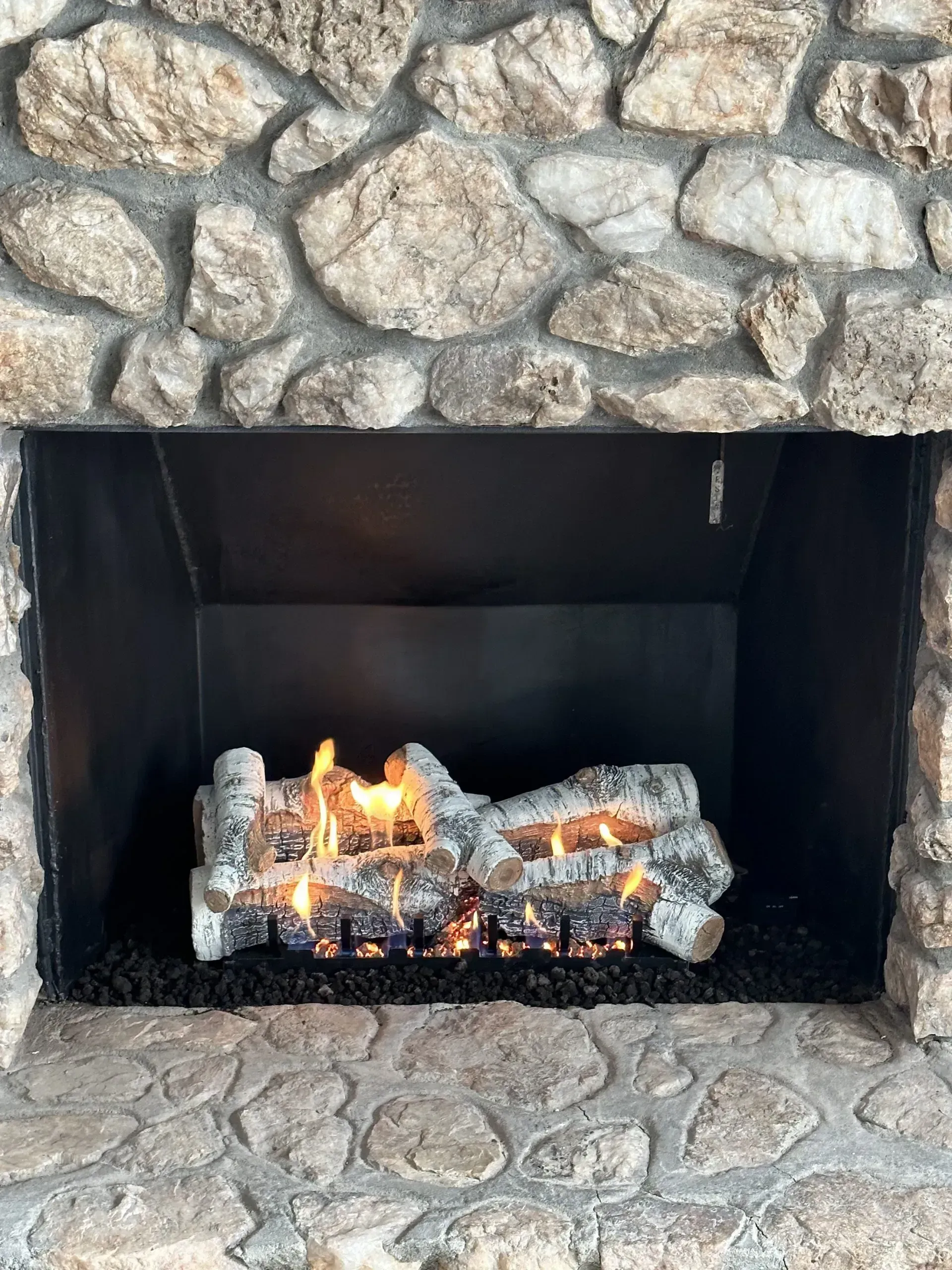 Fireplace with stone surround, lit gas logs in a black firebox.