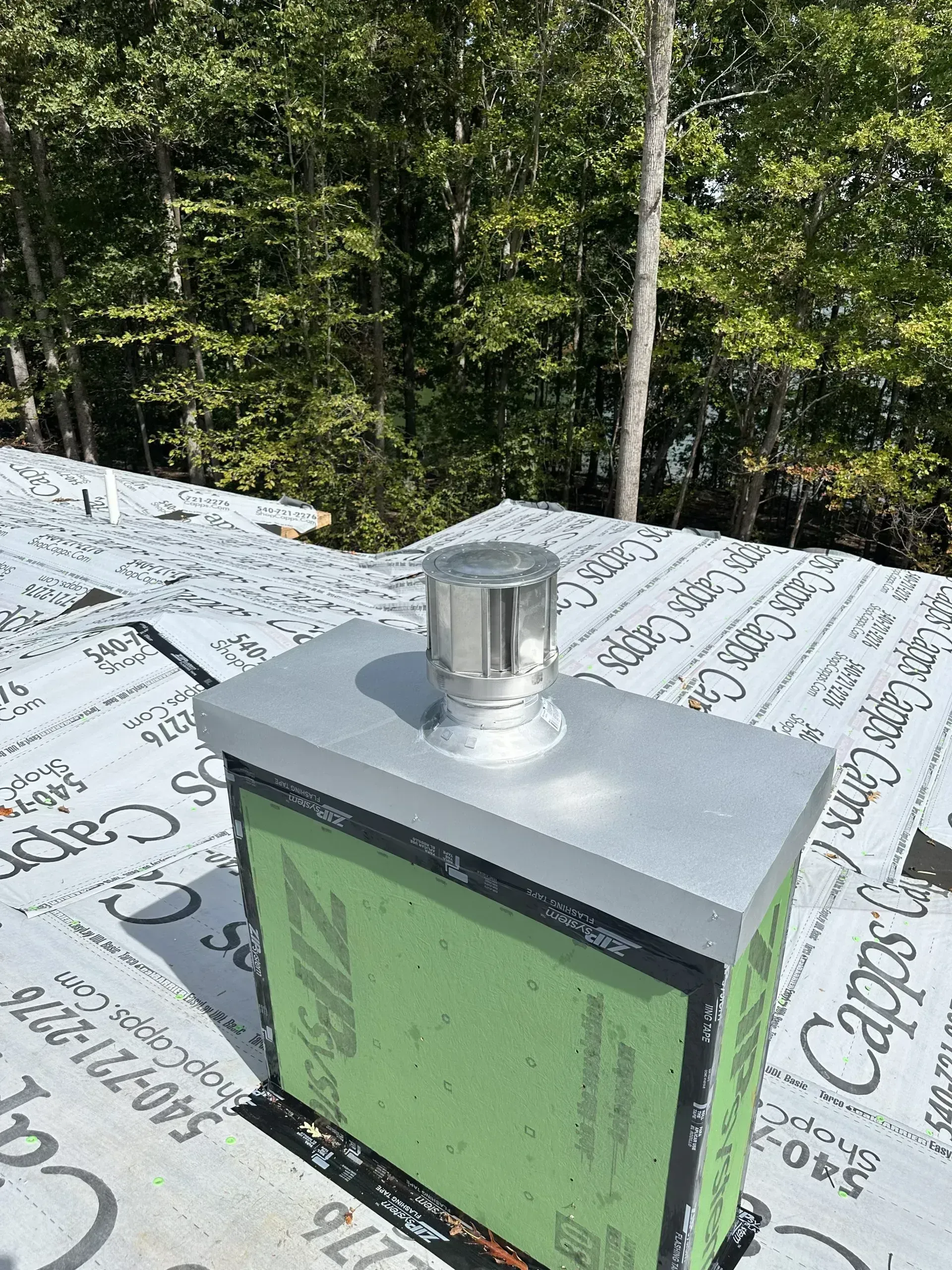 A rooftop vent with a metal cap atop a green, rectangular structure.
