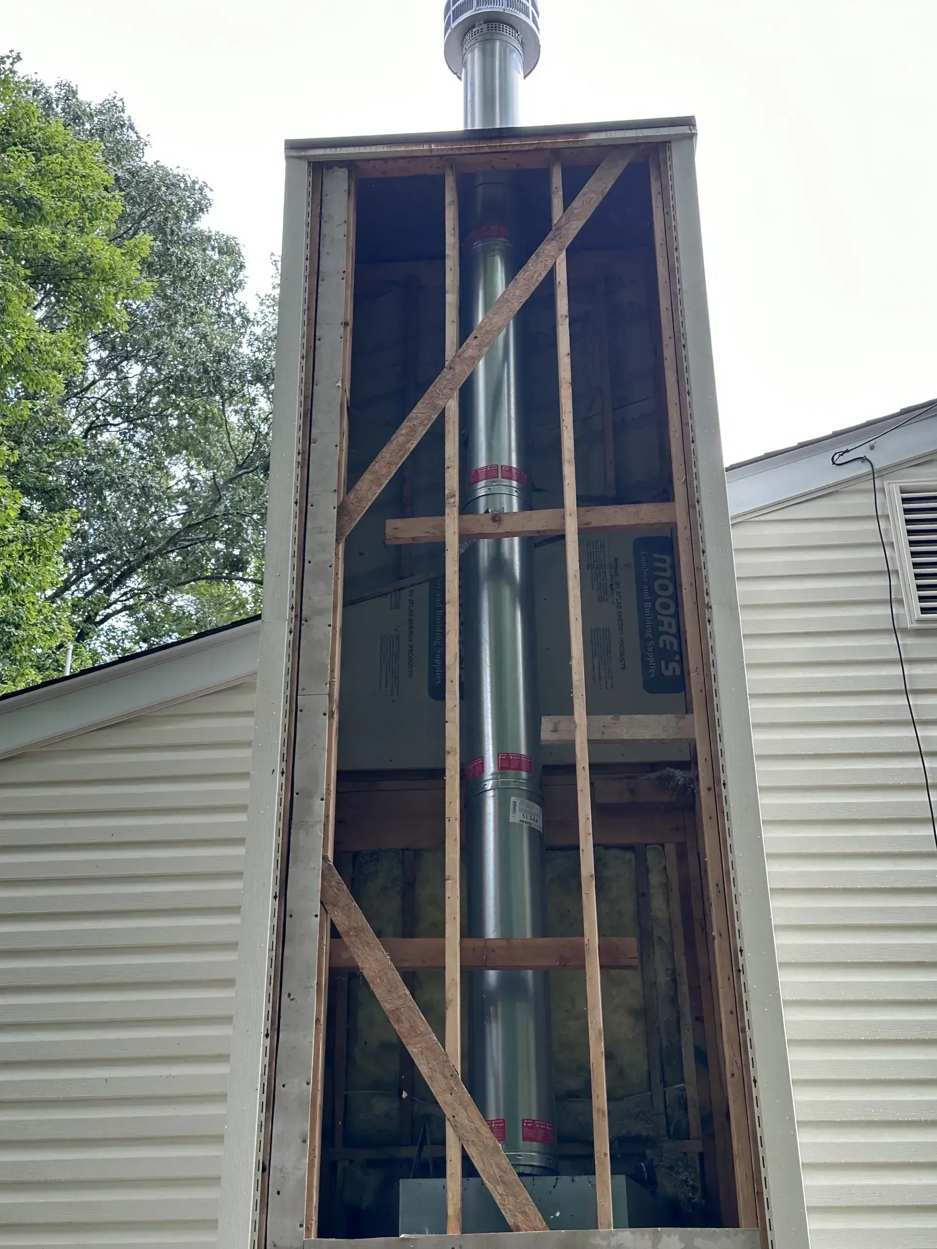 Chimney under construction: A metal flue pipe within a wooden frame, siding visible.