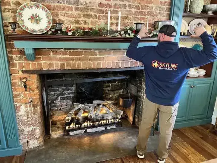 Man with arms raised in front of a fireplace with exposed brick. Blue mantel and cabinetry.