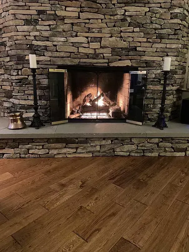 Fireplace with stone surround, lit fire inside. Two candle holders on either side, hardwood floor.