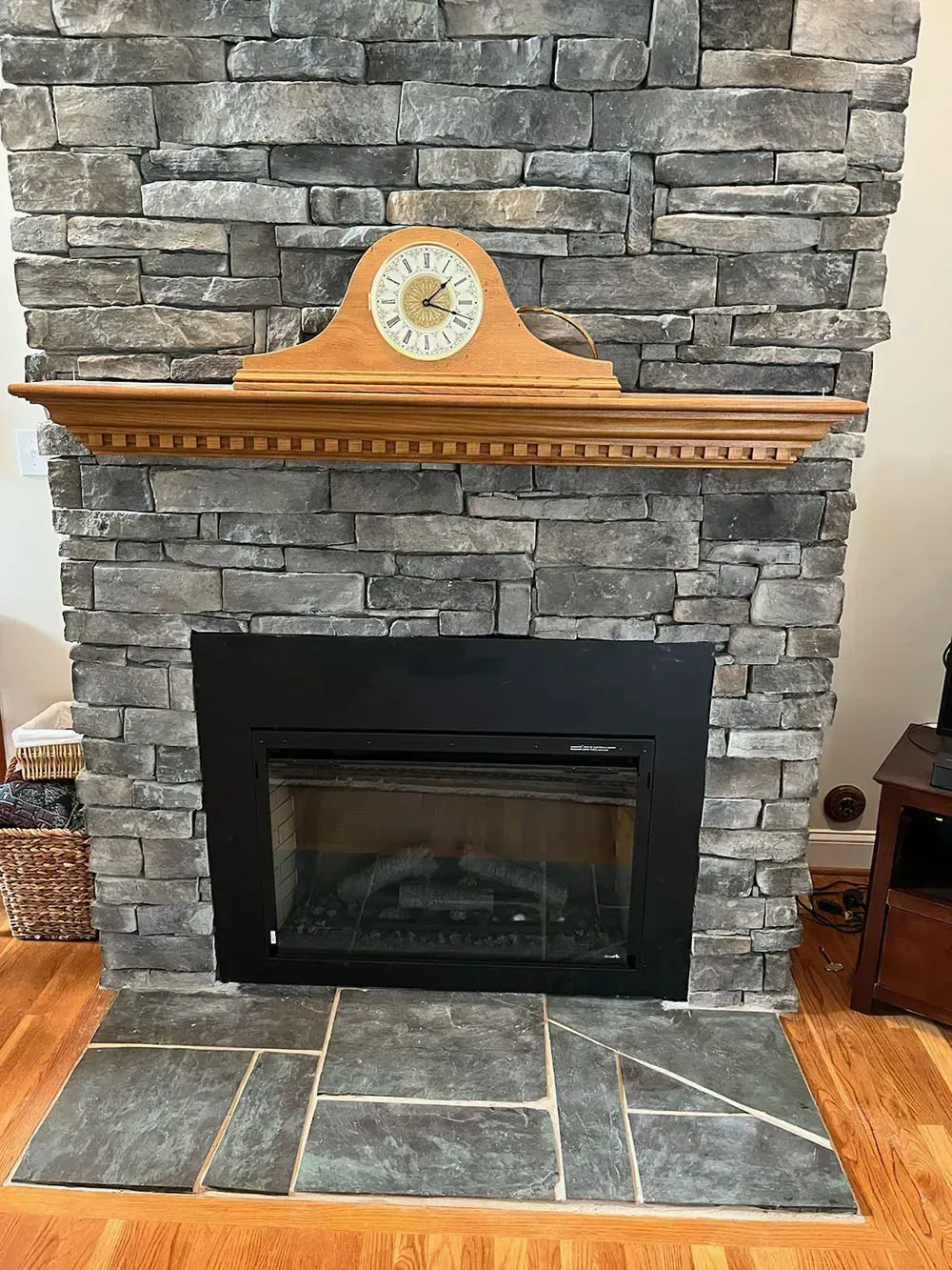 Fireplace with stone facade, dark framed firebox, wood mantel with clock, stone hearth.