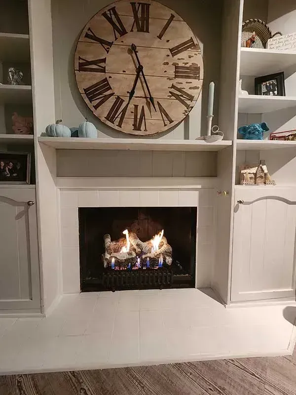 Fireplace with flames, large clock above, built-in shelves with decor.