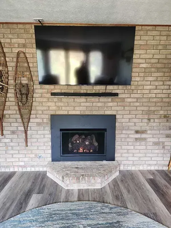Brick fireplace with a TV and soundbar mounted above, flanked by snowshoes on a brick wall.