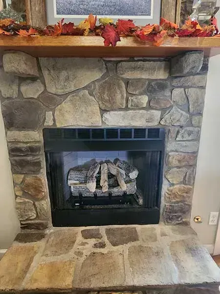 Stone fireplace with wood mantel decorated with fall leaves.