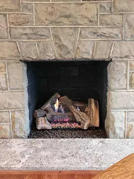Fireplace with stone surround, lit gas logs, and dark interior.