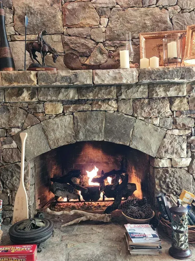 Stone fireplace with fire burning, mantle with candles and decor.